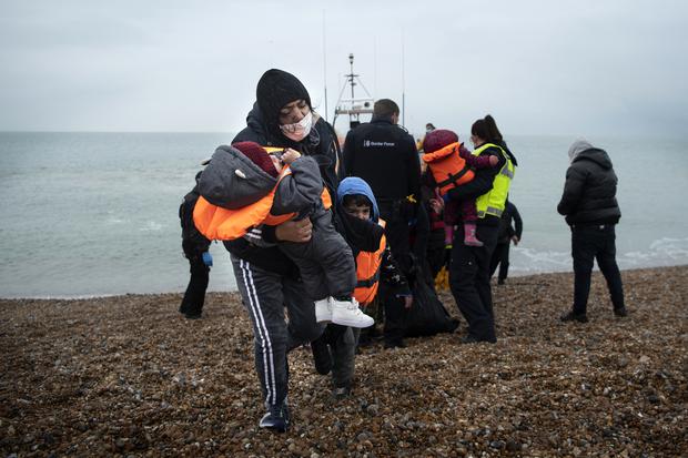 A migrant carries her children after being helped ashore from an RNLI (Royal National Lifeboat Institution) lifeboat on a beach in Dungeness, on the southeast coast of England, on November 24, 2021, after being rescued while crossing the English Channel.  (Photo: Ben STANSALL / AFP).