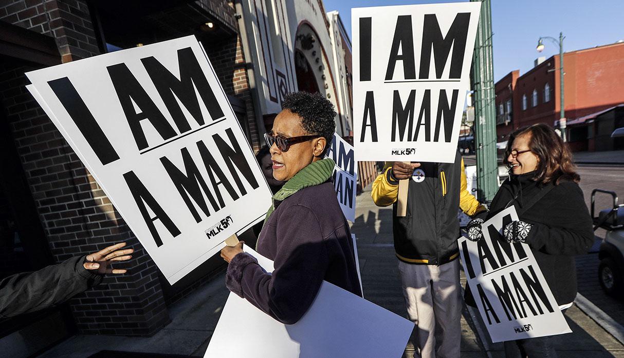Dwania Kyles hands out signs resembling the signs carried by striking sanitation workers in 1968 as people gather for an event commemorating the 50th anniversary of the assassination of the Rev. Martin Luther King Jr. on Wednesday, April 4, 2018, in Memphis, Tenn. King was assassinated April 4, 1968, while in Memphis supporting striking sanitation workers. (AP Photo/Mark Humphrey)