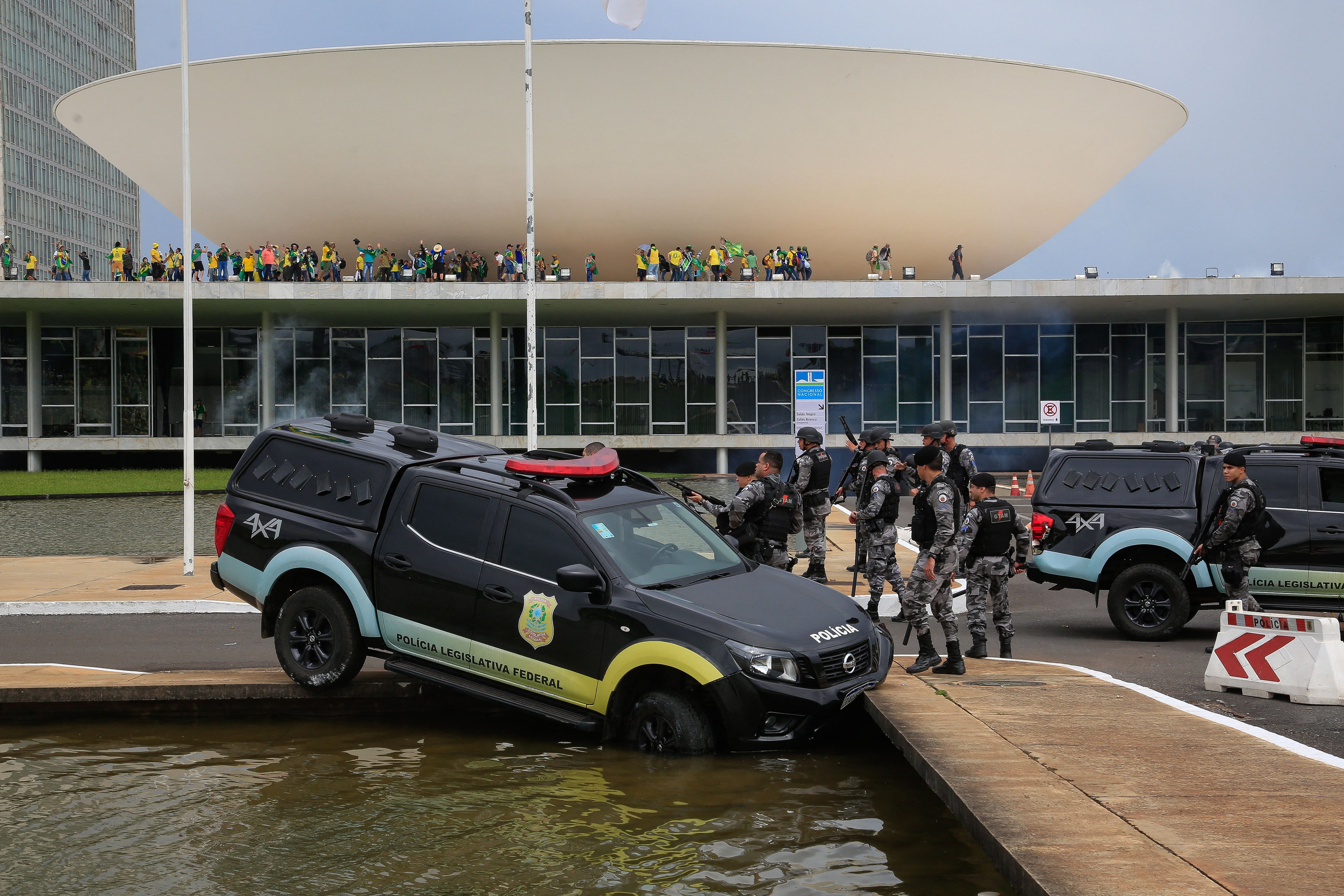 In this file photo taken on January 8, 2023, members of the Federal Legislative Police stand next to a vehicle that crashed into a fountain as supporters of former Brazilian President Jair Bolsonaro invaded the National Congress in Brasilia.