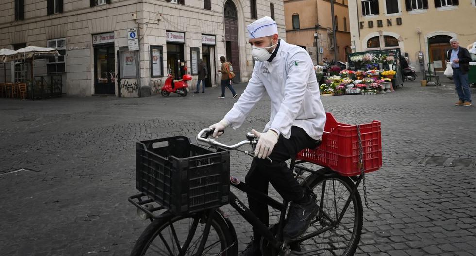 Un cocinero italiano usa una máscara respiratoria como parte de las medidas de precaución contra la propagación del nuevo coronavirus COVID-19, mientras monta una bicicleta en una desierta plaza de Campo Dei Fiori en el centro de Roma. (AFP)