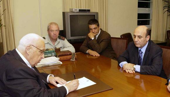 El Primer Ministro israelí, Ariel Sharon, firma la orden de evacuación de los colonos de la Franja de Gaza, mientras el Ministro de Defensa, Shaul Mofaz (D), lo mira en su oficina en Jerusalén el 20 de febrero de 2005. (Foto de AVI OHAYON / GPO / AFP)