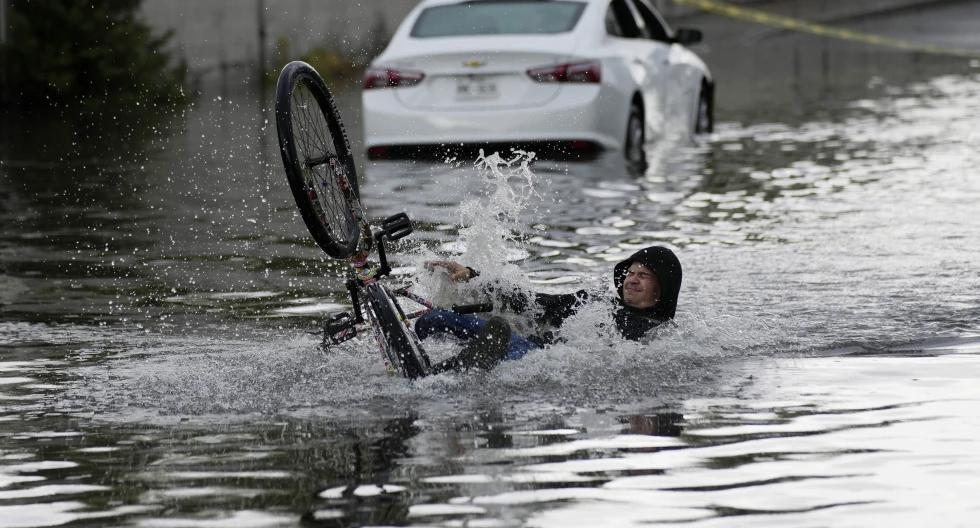 Un ciclista cae mientras intenta atravesar una calle inundada, cerca de un automóvil varado, el viernes 1 de septiembre de 2023, en Las Vegas. (Foto AP/John Locher).