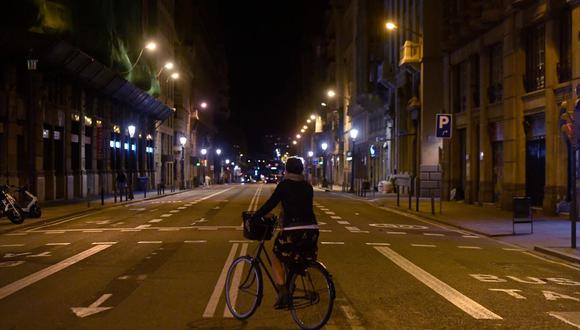 Una mujer anda en bicicleta por una calle desierta en medio de un toque de queda establecido para luchar contra la propagación del COVID-19, en Barcelona el 26 de octubre de 2020. (Josep LAGO / AFP).