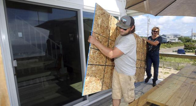 James Masog, en el centro, y Gary Tavares, a la derecha, colocan el tablero de partículas en su lugar para tapar las puertas corredizas de vidrio de la casa de un cliente en Charlestown, RI, antes del huracán Henri. (Foto: AP / Stew Milne)