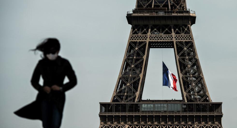 Una mujer con mascarilla facial camina mientras una bandera de Francia ondea en la Torre Eiffel el 11 de mayo de 2020, en plena pandemia de coronavirus COVID-19. (FELIPE LÓPEZ / AFP).