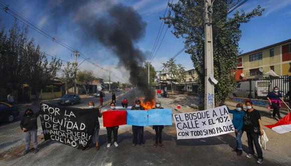 Personas sostienen pancartas cerca de una barricada en llamas durante una protesta en demanda de ayuda económica del gobierno y la aprobación del tercer retiro anticipado de fondos de pensiones en Santiago de Chile, el 22 de abril del 2021. (Foto de RAMON MONROY / AFP).