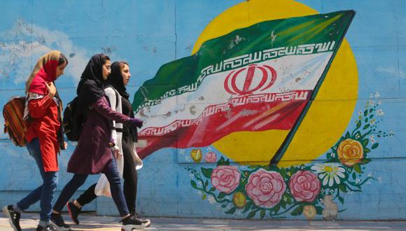 Niñas jóvenes caminan frente a un mural que muestra la bandera nacional iraní en el centro de la capital, Teherán. (Foto: AFP)