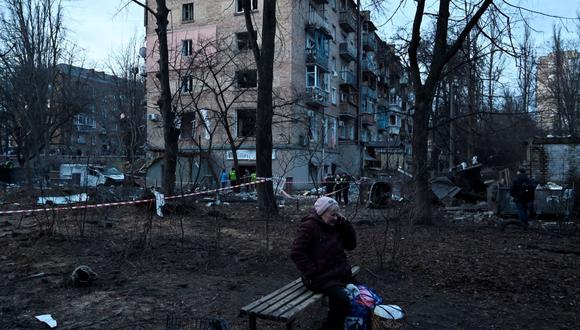 Una mujer habla por teléfono cerca de un cráter dejado por un ataque de Rusia frente a un edificio residencial en Kiev, la capital de Ucrania, el 31 de diciembre de 2022. (SERGEI CHUZAVKOV / AFP).