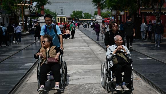 Dos adultos mayores son llevados en sillas de ruedas por sus hijos por las calles de Beijing. Para el año 2100 se calcula que habrán 2.370 millones de personas mayores de 65 años en todo el mundo. AFP / WANG Zhao