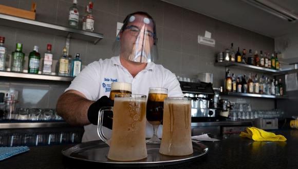 Un camarero con careta prepara unas cervezas para ser servidas en la terraza del bar en la playa de La Malvarrosa en Valencia, España, el 19 de mayo de 2020. (JOSÉ JORDÁN / AFP).