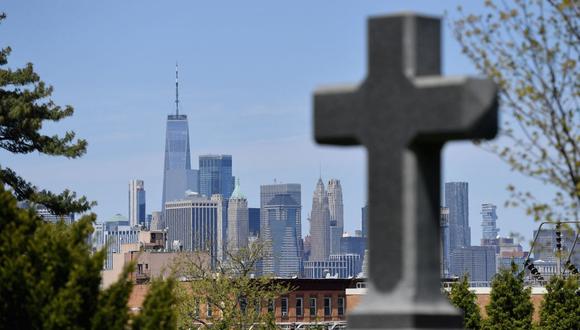 Una tumba con una cruz se encuentra frente al horizonte del bajo Manhattan y la Torre de la Libertad en el cementerio de Greenwood el 5 de mayo de 2020. (Foto de Angela Weiss / AFP).