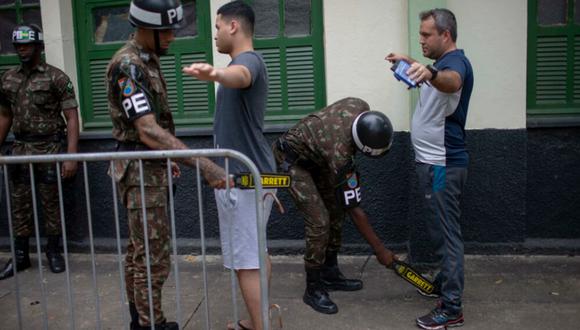 Agentes de la policía federal utilizan un detector de metales para registrar a los votantes, antes de ingresar al colegio electoral, en Río de Janeiro, Brasil.