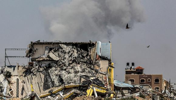 Una columna de humo se eleva detrás de un edificio derrumbado en el lado este del campamento de Maghazi para refugiados palestinos en el centro de la Franja de Gaza el 15 de abril de 2024. (Foto de AFP)