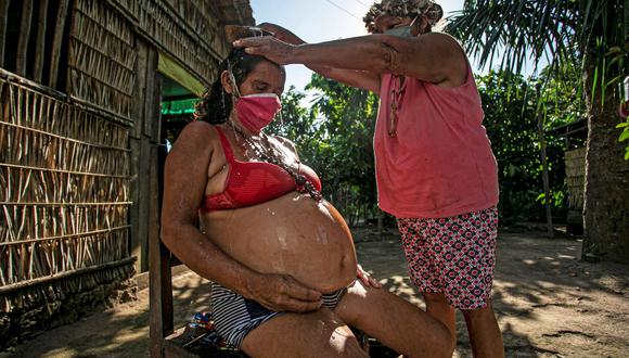 La partera Paje Suzete de la tribu Kumaruara baña a su hija embarazada Celivalda, de 42 años, con hierbas medicinales que cree mantendrán su cuerpo fuerte antes del parto de su bebé de 8 meses en su casa junto al río Tapajos, del municipio de Santarém, en el oeste de Pará, Brasil. (TARSO SARRAF / AFP).