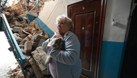 Tamara Skliarova, de 70 años, sostiene un gato frente a los escombros en una escalera de un edificio residencial de dos pisos donde vive, que fue parcialmente destruido como resultado del bombardeo ruso en Kupiansk, región de Kharkiv el 13 de febrero de 2023. (Foto de SERGEY BOBOK / AFP)
