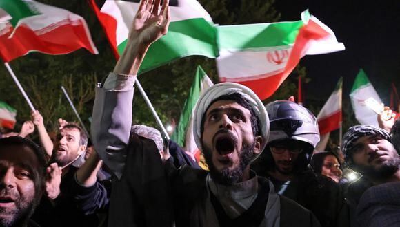 Los manifestantes ondean la bandera de Irán y las banderas palestinas mientras se reúnen frente a la embajada británica en Teherán el 14 de abril de 2024. (Foto de ATTA KENARE / AFP).