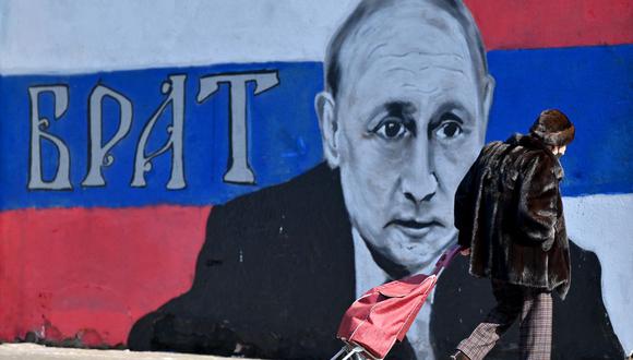 Una mujer pasa frente a un mural que representa al presidente ruso Vladimir Putin, con la palabra "hermano" en la bandera rusa, en Belgrado, Serbia, el 5 de marzo de 2022. (Andrej ISAKOVIC / AFP).