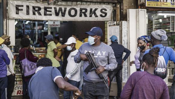 Se ve a un oficial de policía encubierto mientras los clientes hacen cola para comprar fuegos artificiales afuera de la Catedral de Santa María en Johannesburgo, el 30 de diciembre de 2021, antes de las celebraciones de Nochevieja el 31 de diciembre de 2021 (Foto de MARCO LONGARI / AFP).