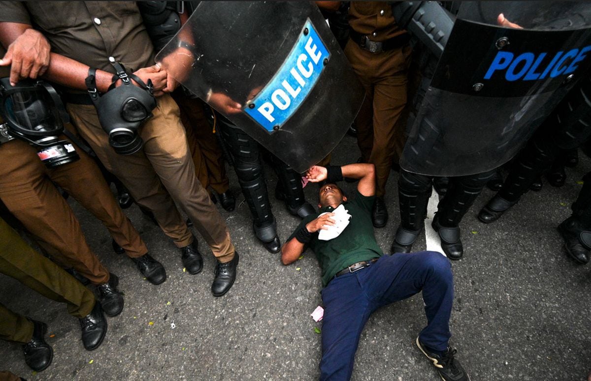 Policemen stand guard and a protester lies on the ground as he takes part in a protest rally against the government demanding the release of university student leaders and against the skyrocketing cost of living, in Colombo on November 2, 2022. (Photo: Ishara S. KODIKARA / AFP)