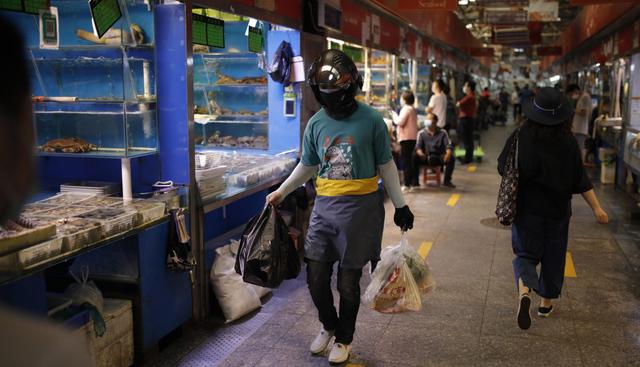 Personas con mascarillas por el coronavirus pasan por los puestos de mariscos en un mercado de Beijing (China). Autoridades continúan en alerta tras brote del COVID-19. (EFE/EPA/STRINGER).