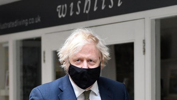 El primer ministro británico, Boris Johnson, que se cubre la cara, pasa frente a una tienda llamada "Wishlist" dentro del mercado de Lemon Street en Truro, Cornualles, en el suroeste de Inglaterra, el 7 de abril de 2021. (JUSTIN TALLIS / various sources / AFP).