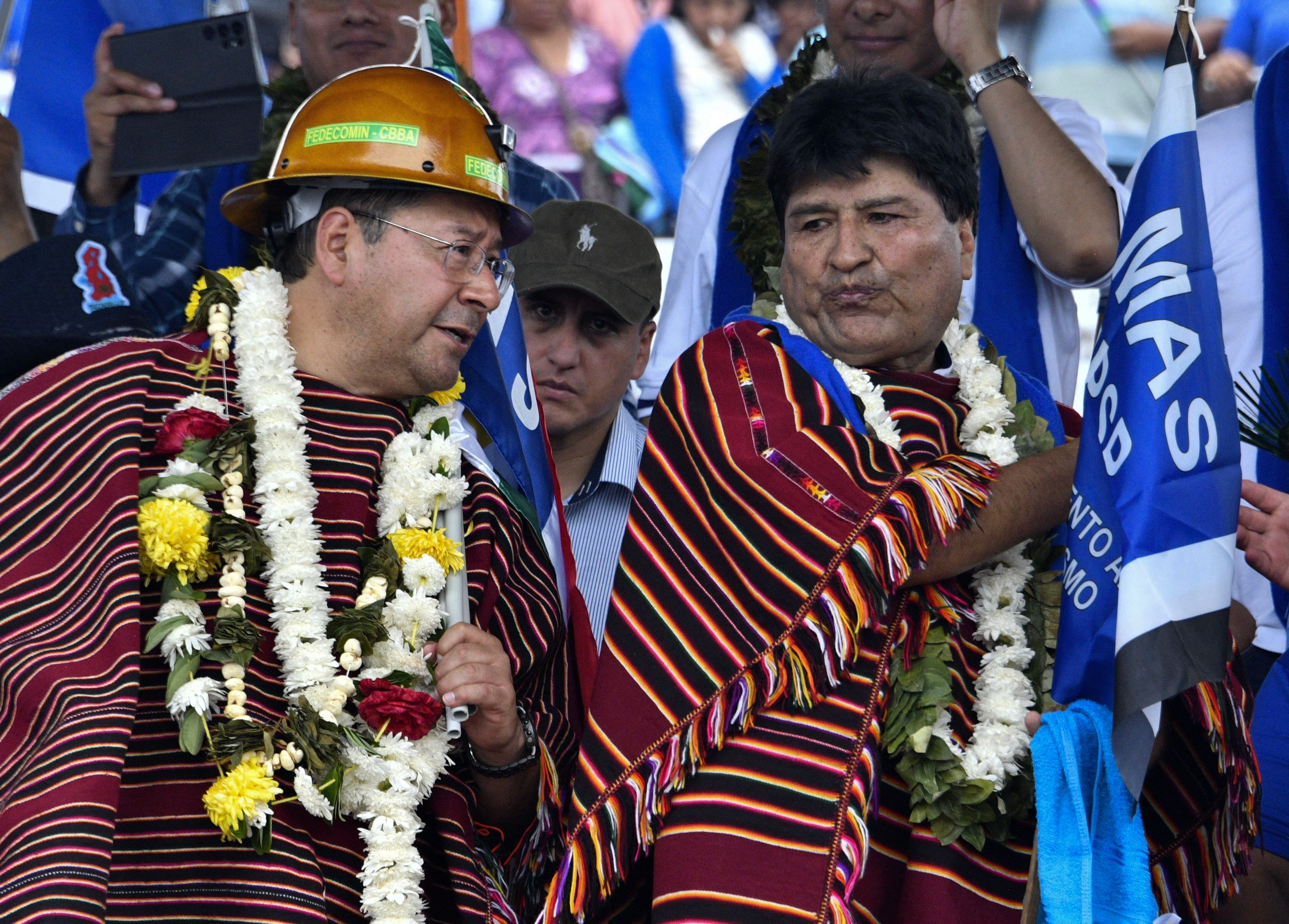 Bolivian President Luis Arce and former President Evo Morales, wearing garlands of flowers and coca leaves, speak during a political meeting to mark the 28th anniversary of MAS, on March 26, 2023. (Photo by Aizar RALDES / AFP).