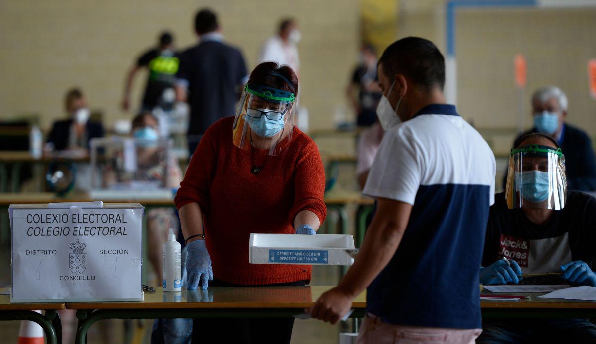 Un hombre que lleva una máscara facial deja su tarjeta de identidad en una bandeja antes de emitir su voto en un colegio electoral en Burela, en el norte de España, durante las elecciones regionales. (AFP/MIGUEL RIOPA).