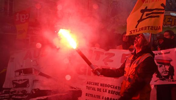 Un manifestante muestra una llamarada roja durante una manifestación el 12 de diciembre de 2019 en París, como parte de una huelga masiva sobre los planes del gobierno para reformar el sistema de pensiones. (AFP)