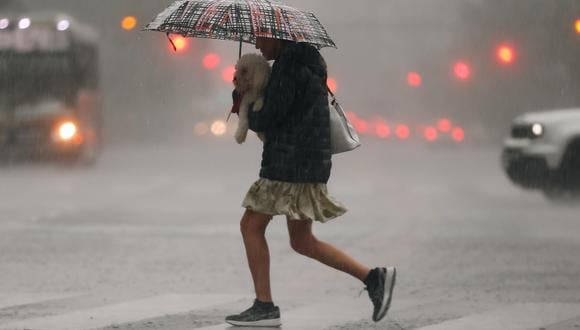 Una mujer carga a su perro mientras corre en medio de la lluvia este miércoles, en Buenos Aires, Argentina. (EFE/ Juan Ignacio Roncoroni).