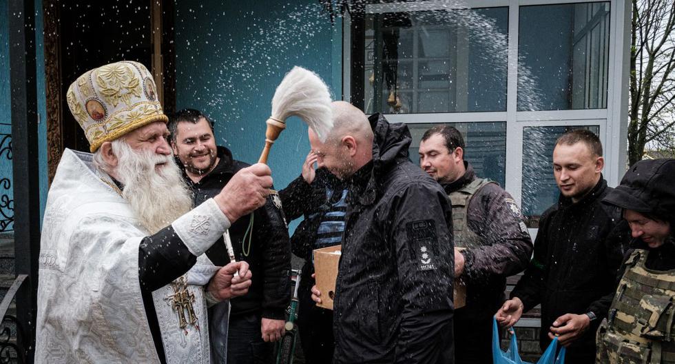 Los oficiales de policía reciben la bendición durante un servicio ortodoxo de Pascua con sonidos continuos de bombardeos a la distancia en la iglesia de San Pedro y San Pablo en Lyman, este de Ucrania, el 24 de abril de 2022. (Yasuyoshi CHIBA / AFP).