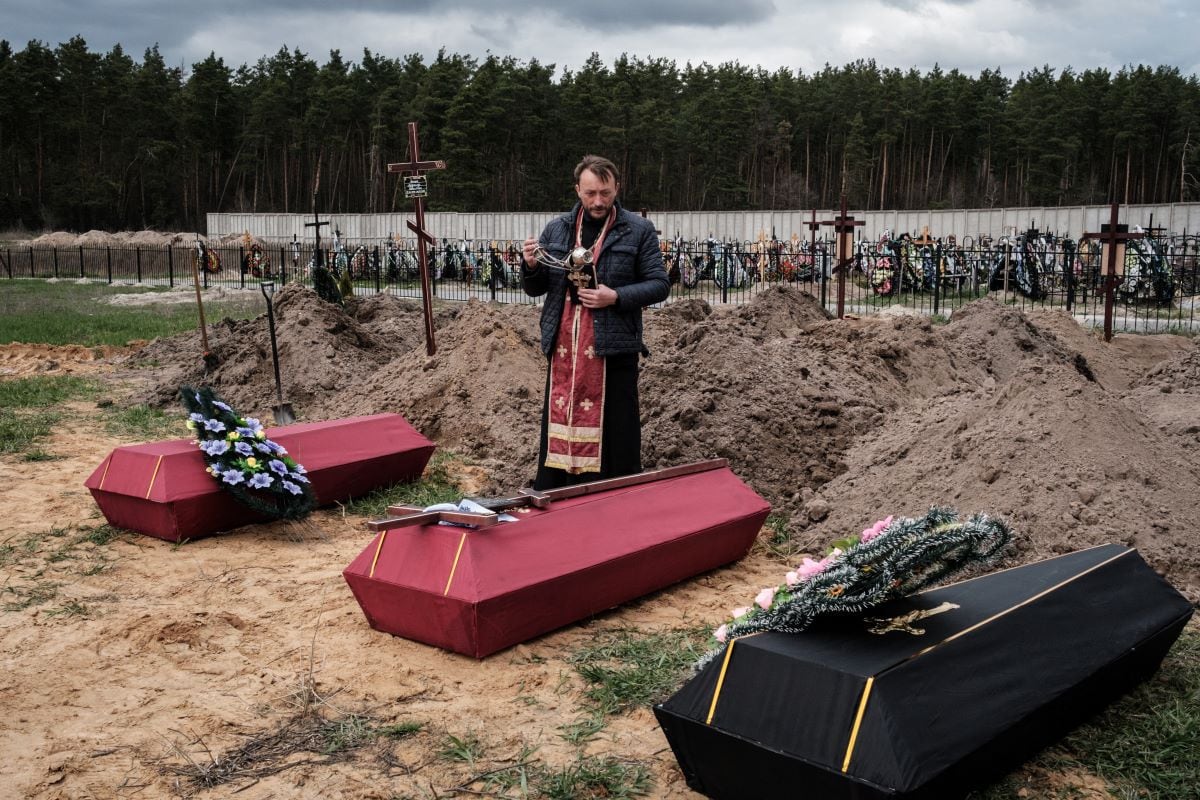 Andrii Holovine, a priest of the Saint Andrew Pervozvannoho Church of All Saints, leads the funeral of three victims at a cemetery in Bucha, on April 18, 2022. (Yasuyoshi CHIBA / AFP)