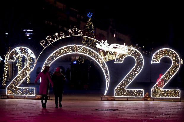 Las mujeres caminan frente a un letrero luminoso de 2022 exhibido en el centro de Pristina el 30 de diciembre de 2021, antes de las celebraciones del Año Nuevo en Kosovo. (Armend NIMANI / AFP).