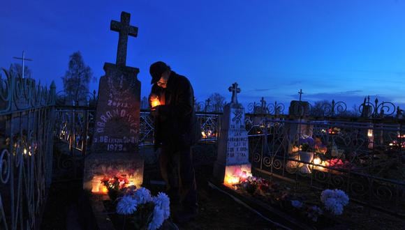 Un hombre coloca una vela en una tumba en un cementerio cerca de la aldea bielorrusa de Baruny. (Foto referencial: VIKTOR DRACHEV / AFP)