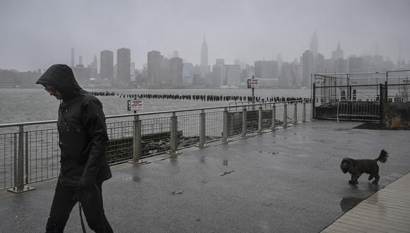 Una persona camina bajo la lluvia y la nieve ante el horizonte de la ciudad de Nueva York en Brooklyn el 14 de marzo de 2023. (Foto de Ed JONES / AFP)