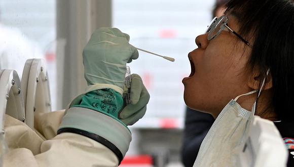 Un trabajador de la salud toma una muestra de un hisopo de una mujer para ser examinada por el coronavirus en Beijing el 28 de octubre de 2021. (Noel Celis / AFP).