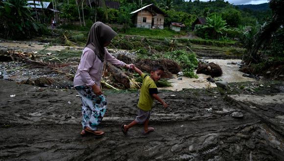 Una mujer y un niño caminan entre los escombros después de una inundación repentina en una aldea en Tangse, provincia de Aceh en Indonesia, el 30 de octubre de 2021. (Foto: CHAIDEER MAHYUDDIN / AFP)
