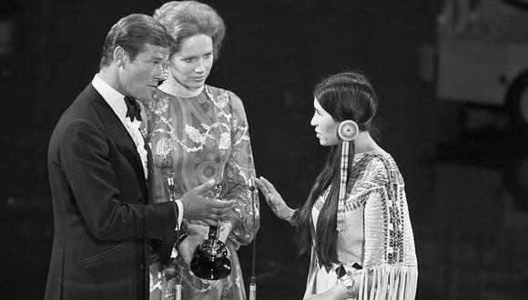 Los actores Roger Moore (izquierda) y Liv Ullman (centro) hacían entrega del premio que fue a recoger Sacheen Littlefeather (derecha), vestida con el traje Apache. (Foto: Getty Images)