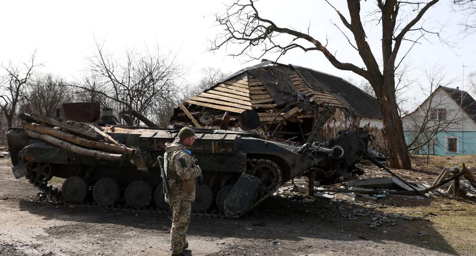 Un soldado ucraniano se para frente a un vehículo blindado de transporte de personal (APC) ruso destruido en una aldea en la línea del frente de la parte norte de la región de Kiev el 28 de marzo de 2022. (Anatolii Stepanov / AFP).