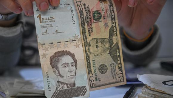 Un hombre exhibe billetes de bolívar y dólares estadounidenses en el mercado municipal de Catia, un barrio de Caracas, el 5 de agosto de 2021. Venezuela eliminará seis ceros de su moneda este viernes. (Federico PARRA / AFP).