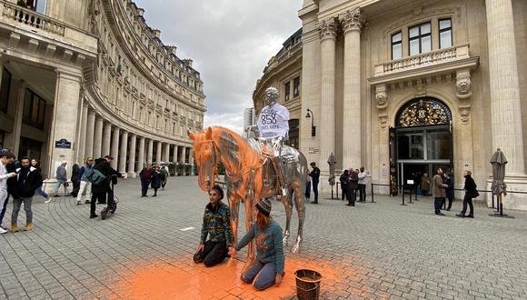 El activista climático del grupo 'Derniere Renovation' se sienta junto a la estatua de Charles Ray "Horse and Rider" después de verterle pintura naranja, afuera del antiguo centro de bolsa, en París, Francia.