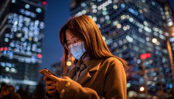 Una mujer que lleva una mascarilla como medida preventiva contra el coronavirus Covid-19 mira su teléfono móvil mientras espera cruzar una calle durante la hora pico en Beijing el 21 de octubre de 2020 (Foto de NICOLAS ASFOURI / AFP).