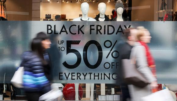 Shoppers pass a promotional sign for 'Black Friday' sales discounts on Oxford Street in London, on November 24, 2017. Black Friday is a sales offer originating from the US where retailers slash prices on the day after the Thanksgiving holiday. In the UK it is used as a marketing device to entice Christmas shoppers with the discounts at stores often lasting for a week. / AFP / Daniel LEAL-OLIVAS
