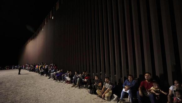 Migrantes esperan junto a un muro fronterizo tras cruzar desde México cerca de Yuma, Arizona. (Archivo)