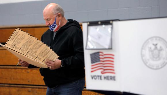 Un hombre con una máscara facial de bandera estadounidense revisa una boleta en un colegio electoral ubicado en el Monseñor John D. Burke Memorial Gym en la Iglesia del Santo Niño en Staten Island, durante la votación anticipada en la ciudad de Nueva York, EE. UU. (Foto: REUTERS / Andrew Kelly).