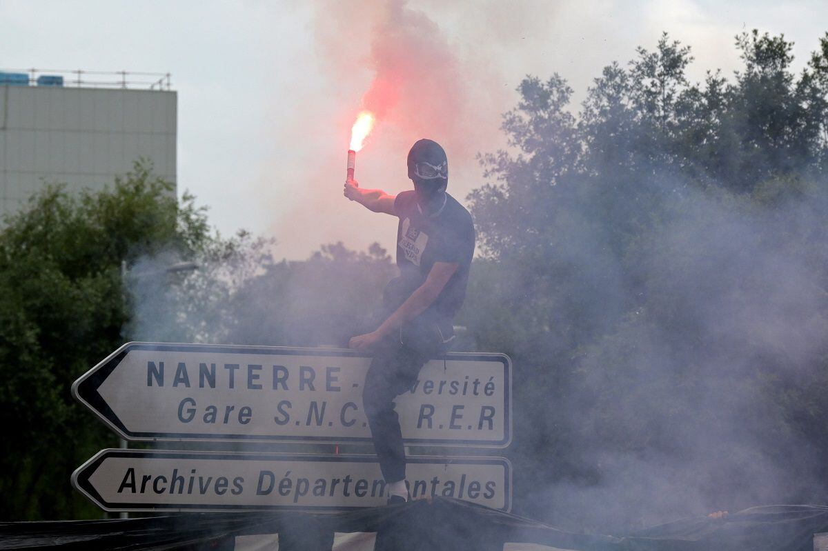 An attendee waves a sparkler as he stands on a street sign during a commemoration march for Nahel, a teenage driver shot dead by a police officer, in Nanterre, on June 29, 2023. (Photo by Alain JOCARD / AFP)