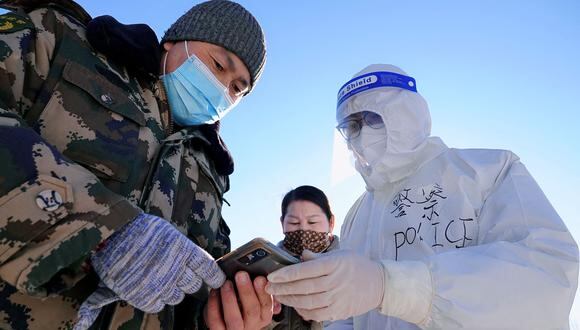 This photo taken on December 4, 2021 shows a police officer wearing personal protective equipment (PPE) guiding residents to undergo nucleic acid tests for the Covid-19 coronavirus, in Hulun Buir in China's northern Inner Mongolia region. (Photo by AFP) / China OUT