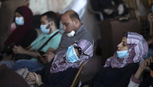 Fotografía de archivo del 27 de septiembre de 2020 de palestinos con mascarillas sentados junto a su equipaje mientras esperan cruzar el cruce fronterizo con Egipto Rafah en el sur de la Franja de Gaza. (AP Foto/Khalil Hamra, Archivo).