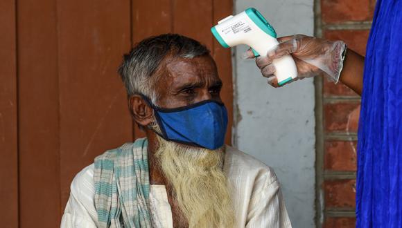 Un trabajador sanitario mide la temperatura corporal de un paciente infectado con lepra como parte de un chequeo general realizado el 11 de octubre de 2020 con el fin de detectar casos de coronavirus en la India. (Foto de SAM PANTHAKY / AFP).