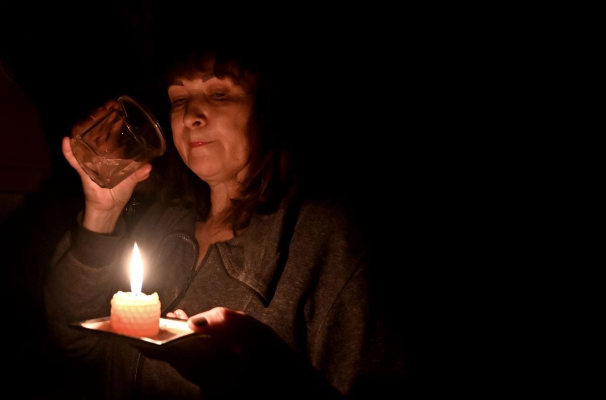 This photograph taken on November 5, 2022 shows Iren Rozdobudko, a 60-year-old writer and university professor, drinking a glass of water by candlelight during a power outage in kyiv.  (SERGEI SUPINSKY / AFP).