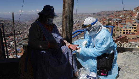 Un trabajador de la salud vestido con equipo de protección completo extrae sangre de una mujer para realizar la prueba del nuevo coronavirus durante una campaña de pruebas de casa en casa en el barrio de Villa Rosasani de La Paz, Bolivia, el viernes 28 de agosto de 2020. (AP Foto/Juan Karita).